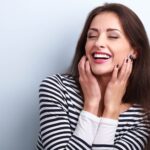 Brunette woman in a striped shirt smiles after professional teeth whitening in Dallas, TX